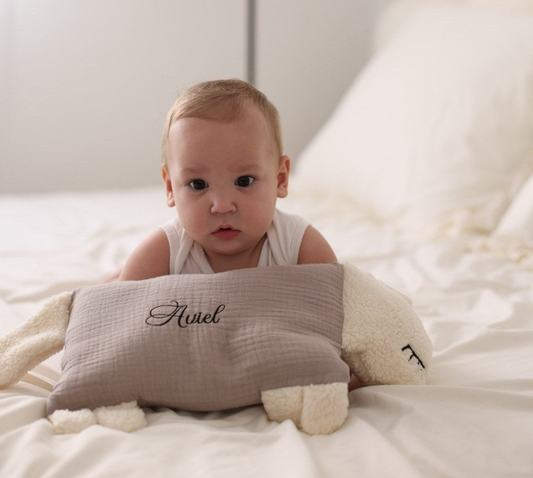Baby mit seinem Kuschelschaf, auf dem der Name Ariel gestickt ist