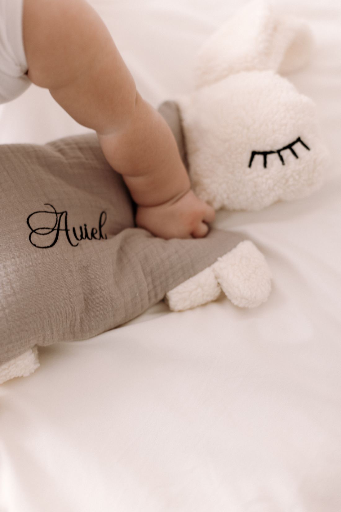 Babyhand auf einem Kuscheltier mit dem eingestickten Namen Ariel